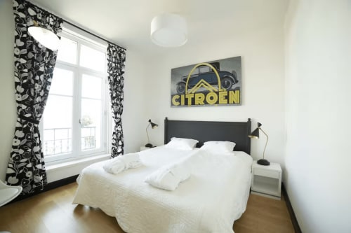 Chambre lumineuse de la Gare Godillot B&B à Saint-Ouen avec rideaux à motifs noirs, linge blanc et art mural Citroën vintage.