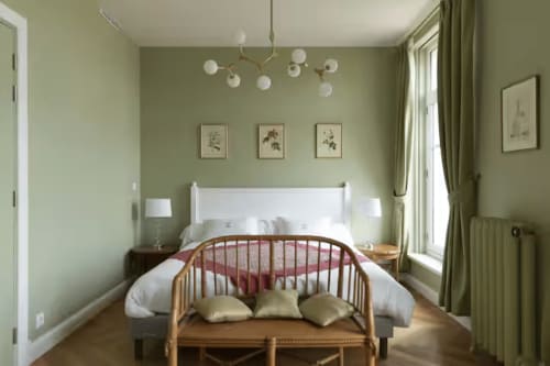 Chambre apaisante aux tons sauge à la Gare Godillot BnB, avec tête de lit blanche, banc en bois et art botanique.