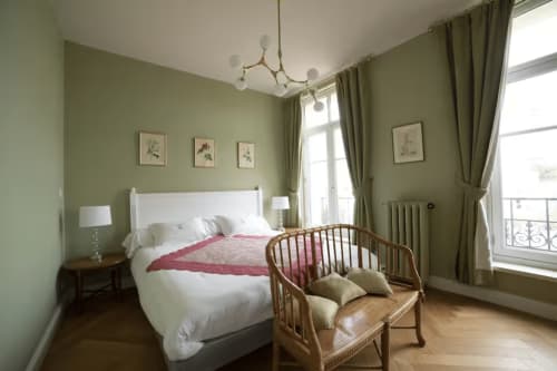Chambre Gare Godillot à Saint-Ouen aux murs vert sauge, lit blanc, chaise en bois et vue sur balcon parisien.