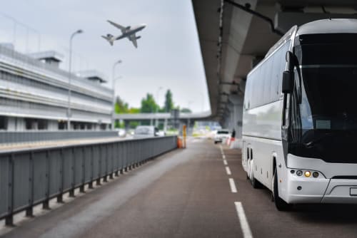Autobus navetta bianca all'area di ritiro dell'aeroporto vicino a Villapiana con aereo in decollo sopra