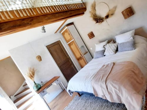 Chambre sous les combles cosy au Petit Bégou avec poutres en bois, murs blancs et literie neutre.