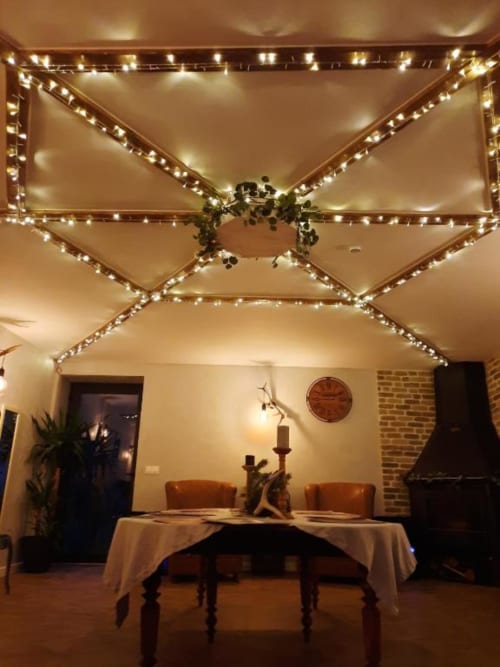 Salle à manger élégante du Petit Bégou avec guirlandes lumineuses formant des motifs en X au plafond et table décorée