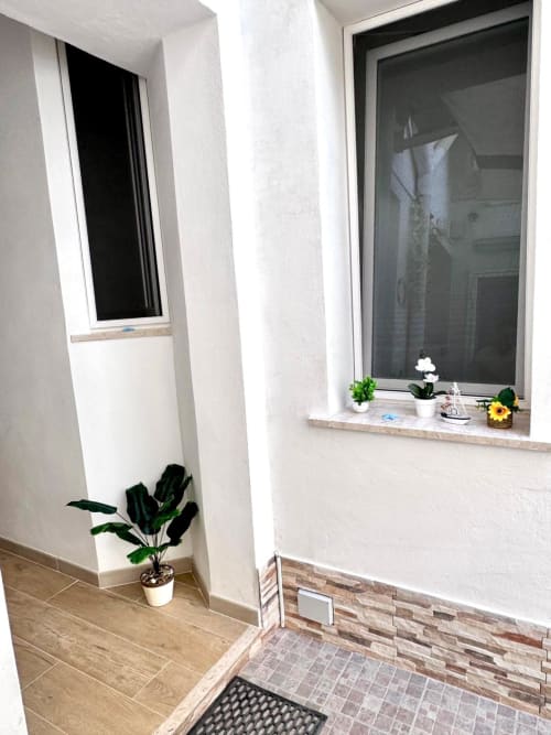 Bright entryway at Casa Vacanze La Coccinella in Trapani with potted plants, window with shutters, and tiled flooring