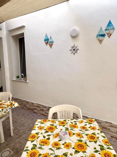 Dining area in Casa Vacanze La Coccinella apartment with sunflower-patterned tables, white chairs, and nautical-themed wall