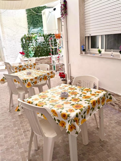Outdoor patio dining area at Casa Vacanze La Coccinella in Trapani with white plastic chairs and sunflower-patterned