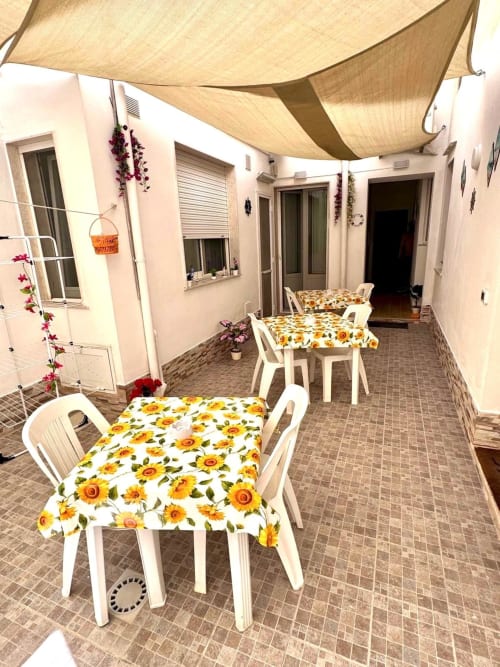 Sunny courtyard patio at Casa Vacanze La Coccinella in Trapani with white chairs, sunflower cushions, and shade sail