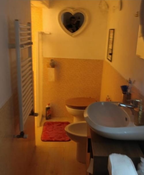 Bagno di Vaticangardenflat a Roma con lavabo bianco, toilette, tappeto rosso, specchio a forma di cuore e illuminazione calda