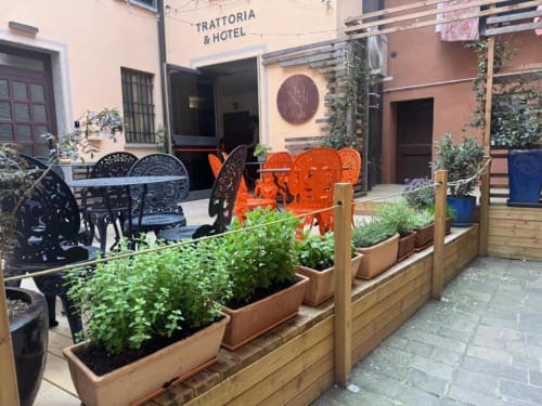 Cortile di Trattoria & Hotel a Vergato con sedie arancioni, sedute nere e piante in vaso