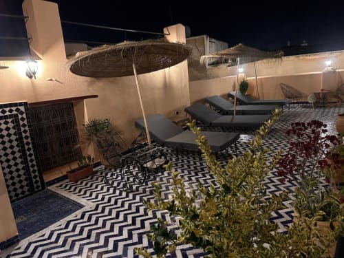 Terrasse sur le toit du Riad Dar Tahri à Fès avec lits de repos, parasols de chaume et carrelage marocain de nuit