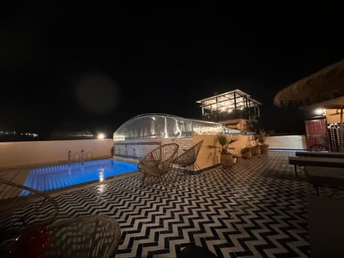 Piscine sur le toit la nuit au Riad Dar Tahri à Fès, Maroc, avec eau illuminée en bleu, chaises longues et vue sur la ville
