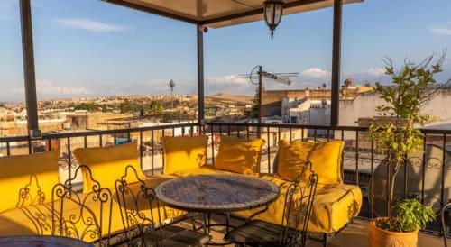 Terrasse sur le toit du Riad Dar Tahri à Fès avec sièges aux coussins jaunes, table en mosaïque et vue sur la médina