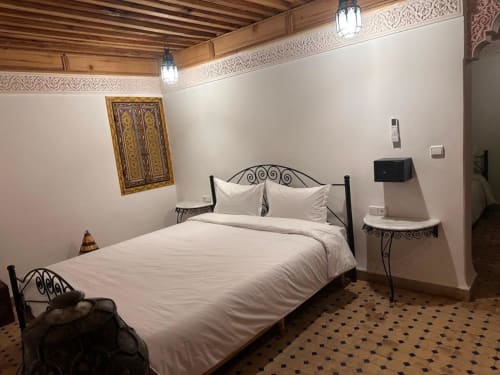 Chambre marocaine traditionnelle au Riad Dar Tahri à Fès avec lit en fer forgé, lin blanc, plafond bois ouvragé