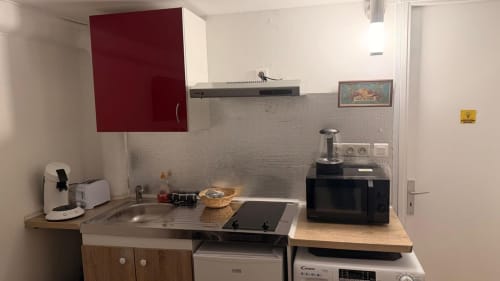 Kitchenette de l'appartement Kawichimmo Louvres avec meubles bordeaux, cuisinière, micro-ondes et cafetière
