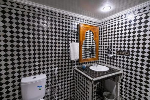 Salle de bains à carreaux noirs et blancs du Riad Fes Aicha avec lavabo, toilettes et miroir orné avec porte-serviettes