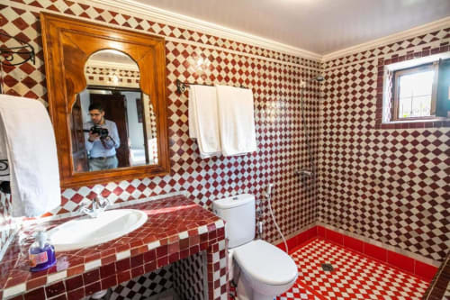 Salle de bains carrelée rouge et blanc avec lavabo, toilettes et miroir encadré en bois au Riad Fes Aicha à Fès, Maroc