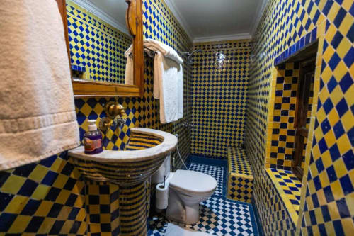 Salle de bain marocaine aux carreaux bleus et jaunes vibrants, lavabo et toilettes rayés au Riad Fes Aicha à Fès
