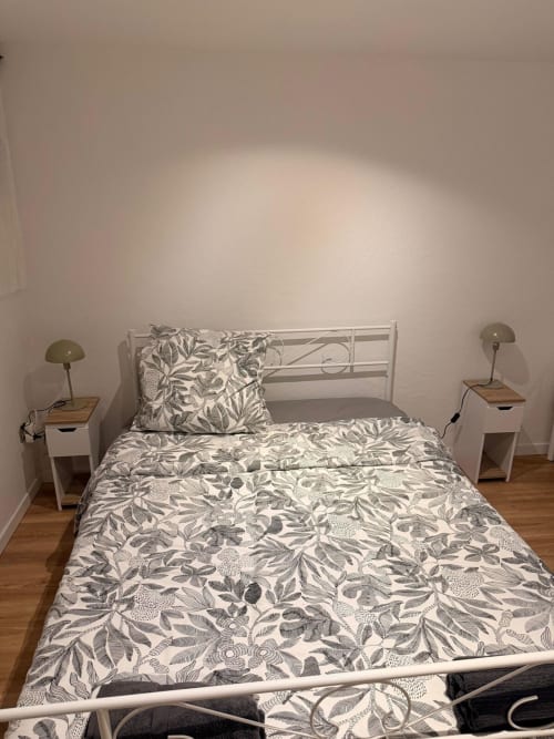 Chambre lumineuse de l'appartement Kawichimmo Louvres avec literie à motifs, lit en métal blanc et tables de nuit avec lampes