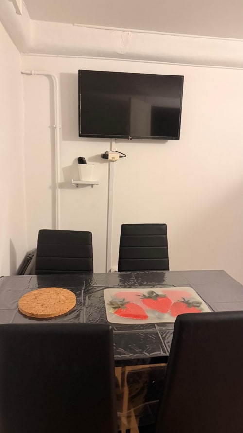 Coin repas de l'appartement avec télévision écran plat, chaises sombres, sets de liège et fraises sur la table à Kawichimmo Locations