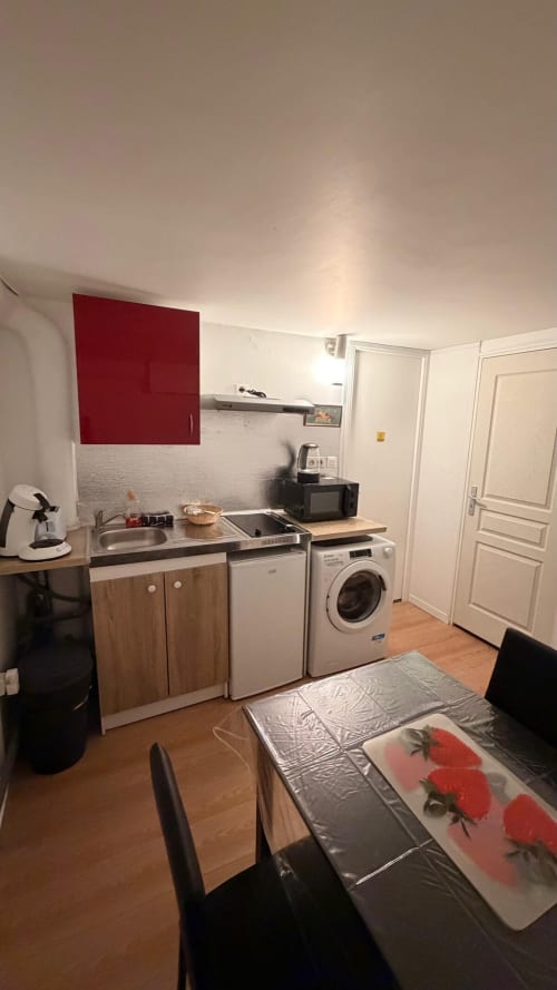 Cuisine compacte d'un appartement T2 à Louvres avec placards rouges, cuisinière, lave-linge et table à manger