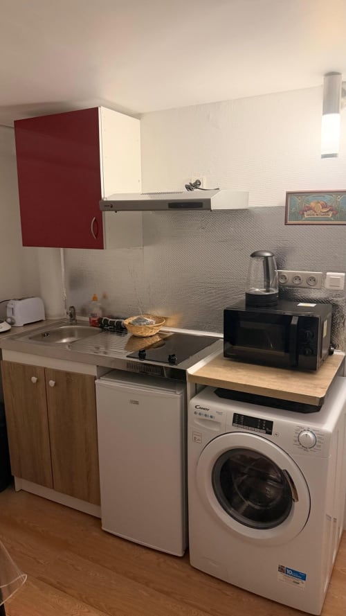 Petite cuisine de l'appartement à Louvres avec armoire rouge, cuisinière, lave-linge et micro-ondes