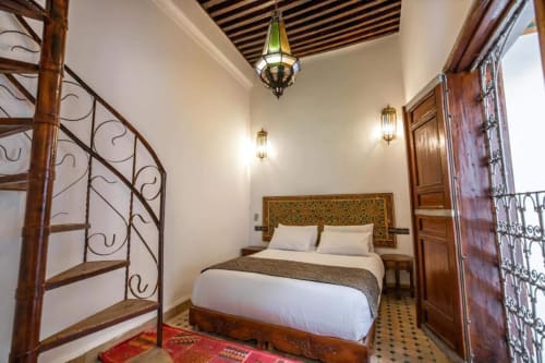 Chambre marocaine au Cèdre d'Argent à Fès avec poutres en bois, tête de lit ornementée et luminaire suspendu vert