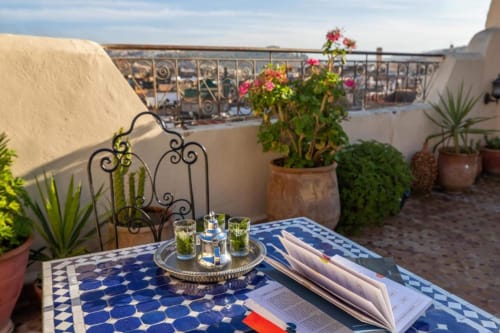 Terrasse sur le toit du Cèdre d'Argent à Fès avec table en mosaïque bleue, plantes en pots et vue sur la ville