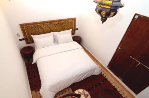 Chambre de style marocain à l'hôtel Le Cedre D'argent à Fès avec tête de lit ornementée, literie blanche et décoration traditionnelle