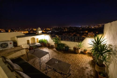 Terrasse sur le toit de l'hôtel Le Cèdre D'argent à Fès avec vue nocturne sur la ville, espace de détente et plantes en pot