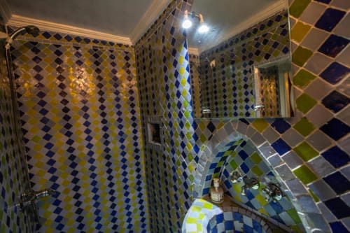 Carrelage de salle de bain aux motifs de losanges bleu vif, jaune et vert à l'hôtel Le Cèdre d'Argent à Fès, avec équipements de douche et