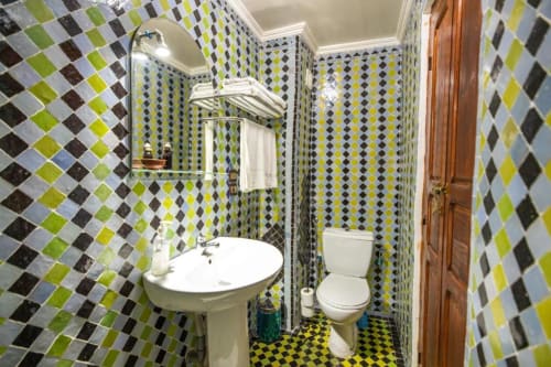 Salle de bains carrelée colorée au Cèdre d'Argent à Fès avec motifs mosaïques géométriques, lavabo sur piédestal et toilettes