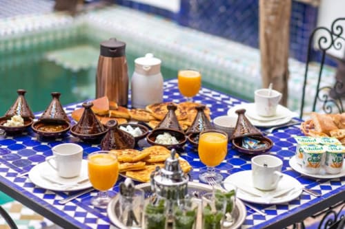 Table de petit-déjeuner marocain avec tajines, pâtisseries et jus d'orange surplombant la piscine au Cèdre d'Argent à Fès