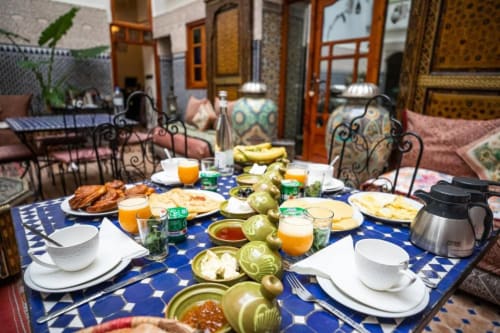 Petit-déjeuner au Riad Dar Tahri à Fès avec pâtisseries, fruits frais, jus et couverts sur table bleue à motifs
