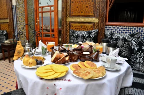 Petit-déjeuner marocain traditionnel au Riad Dar Tahri à Fès : crêpes, pâtisseries, fruits et thé dans une cour ornée