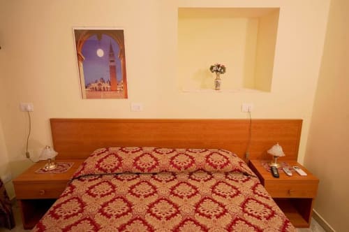 Camera da letto accogliente di Parioli House Roma con letto in legno, biancheria rossa fantasia e decori con stampe veneziane