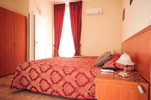 Camera da letto accogliente a Parioli House B&B a Roma con biancheria rossa a motivi, tende coordinate e testata arancione