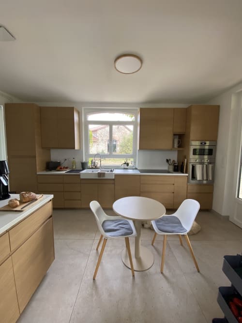 Cuisine moderne et salle à manger avec mobilier en chêne, table ronde blanche et vue sur le jardin du gîte Le Domaine les Olivoux