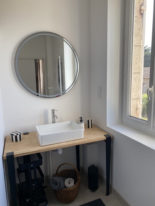 Lavabo moderne avec vasque blanche et miroir rond au gîte Le Domaine les Olivoux à Pomport