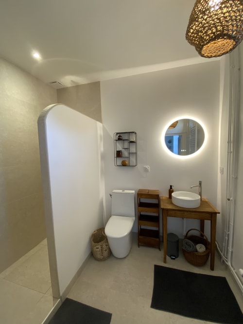 Salle de bain moderne du Domaine les Olivoux à Pomport avec miroir rond, meuble-lavabo en bois et toilettes blanches