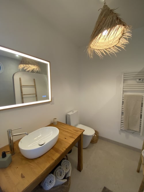 Salle de bain moderne au gîte Le Domaine les Olivoux à Pomport avec vanité en bois, lavabo blanc, toilettes et luminaire tressé décoratif