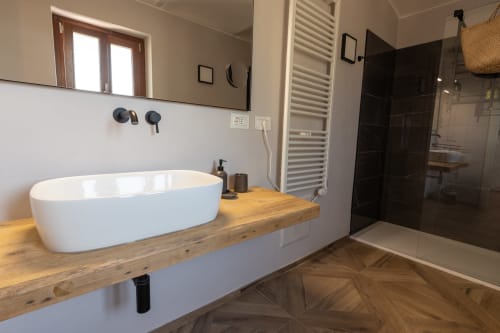 Bagno moderno nella Casa Miravigne con lavabo bianco su mobile in legno, box doccia nero e scaldasalviette
