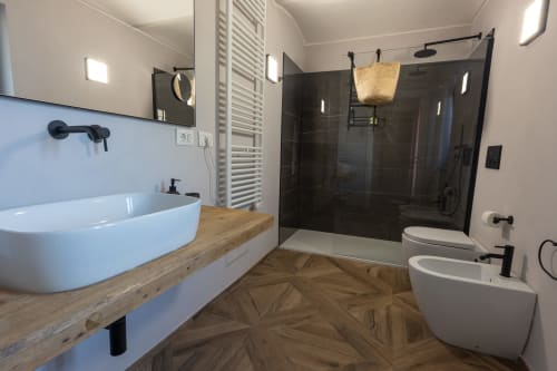 Bagno moderno con lavabo bianco a coppa, mobile in legno, doccia a pioggia nera e pavimento geometrico in legno di Miravigne House