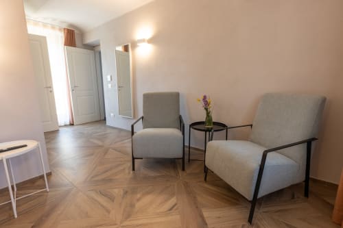 Elegante zona lounge di Miravigne House con due poltrone grigie, tavolino con fiori, pavimenti in legno a spina di pesce e vista panoramica