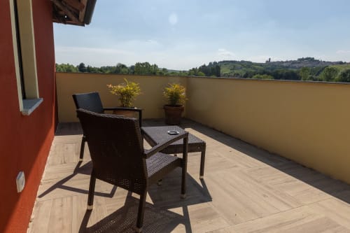 Terrazza soleggiata della Casa Miravigne con lettino nero, piante in vaso e vista sulla campagna di Castagnole delle Lanze