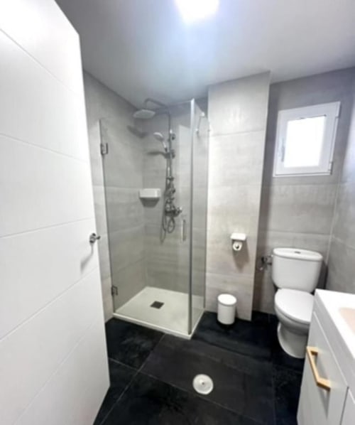 Baño moderno en Apartamento Jacaranda de ROILA360 Alicante con ducha a ras de suelo, inodoro y baldosas negras
