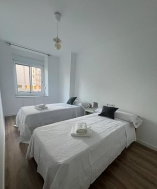 Dos camas individuales con sábanas blancas en la luminosa habitación del Apartamento Jacaranda del hotel ROILA360 en Alicante con vistas al jardín