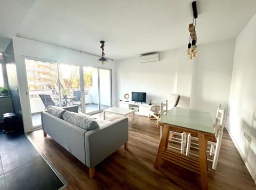 Sala de estar del Apartamento Jacaranda en Alicante con sofá gris, mesa de comedor, TV, acceso a terraza y vistas al jardín