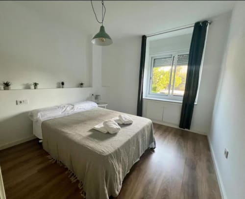 Dormitorio moderno en Apartamento Jacaranda, Alicante con vistas al jardín, suelos de madera, lámpara colgante y acceso a terraza