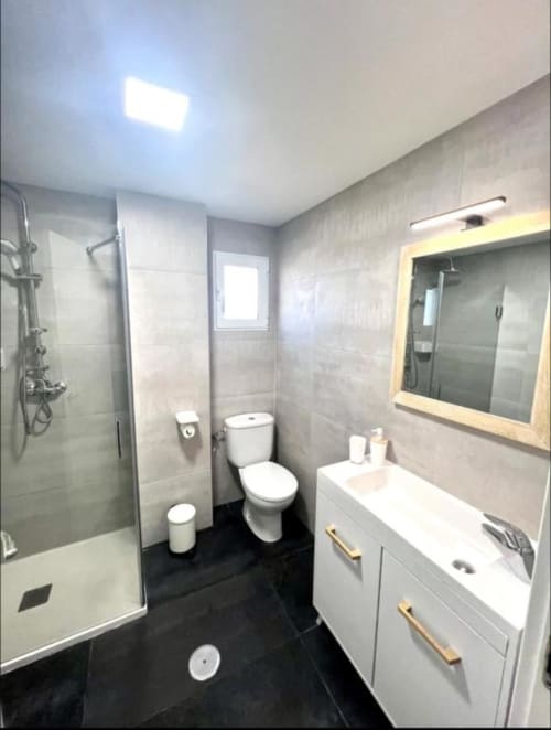 Baño moderno en Apartamento Jacaranda de ROILA360 Alicante con ducha a ras de suelo, WC, tocador blanco y espejo