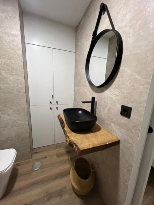 Baño moderno en apartamento ROILA360 Alicante con lavamanos negro sobre mueble de madera rústica y espejo redondo negro