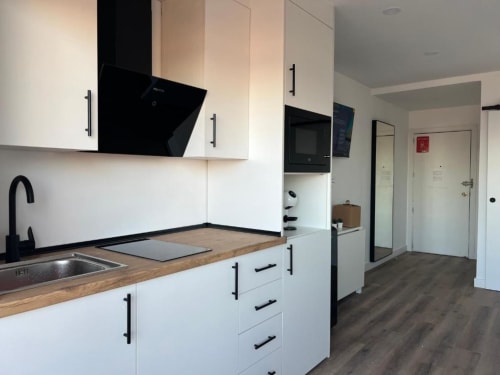 Cocina moderna blanca con encimera de madera, electrodomésticos negros y tiradores en apartamento de Alicante